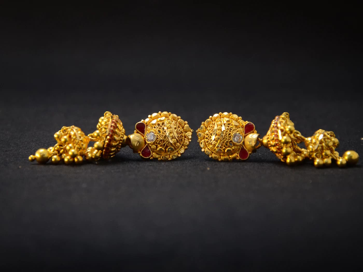Gold stud earrings with jhumka drops on a dark surface (illustrative photo)